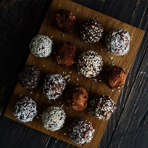 no bake chocolate peppermint balls with crushed candy canes and coconut flakes on the outside, sitting on a cutting board